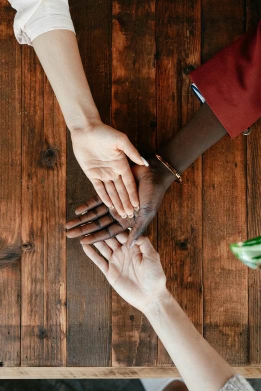 a group of people putting their hands together, trending on pexels, renaissance, sitting on a mocha-colored table, two people, ( ( dark skin ) ), on wooden table