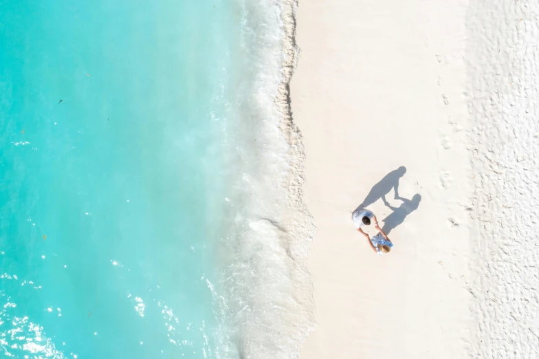 a couple of people standing on top of a sandy beach, pexels contest winner, minimalism, carribean turquoise water, overhead sun, lying down, white hue