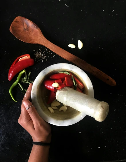 a person holding a wooden spoon over a bowl of food, mortar and pestle, all marble, assamese, profile image