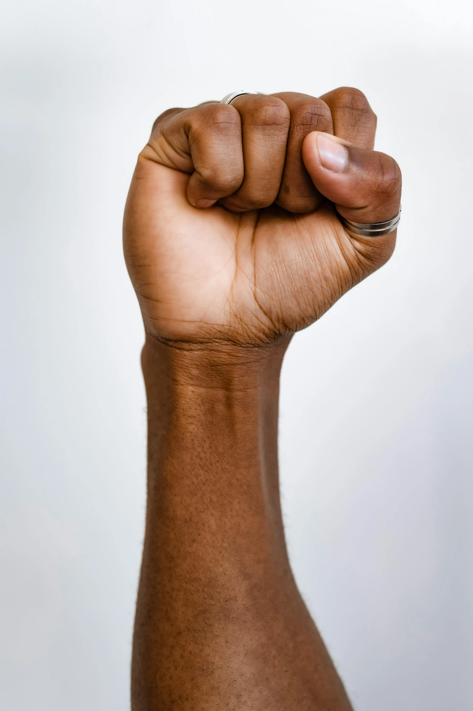a close up of a person's arm with a ring on it, symbolism, raised fist, brown skin, on a gray background, brown