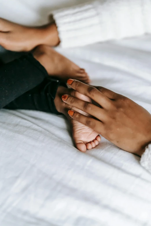 a man and a woman holding hands on a bed, by Victorine Foot, trending on pexels, babies in her lap, black young woman, lesbian, focus on his foot