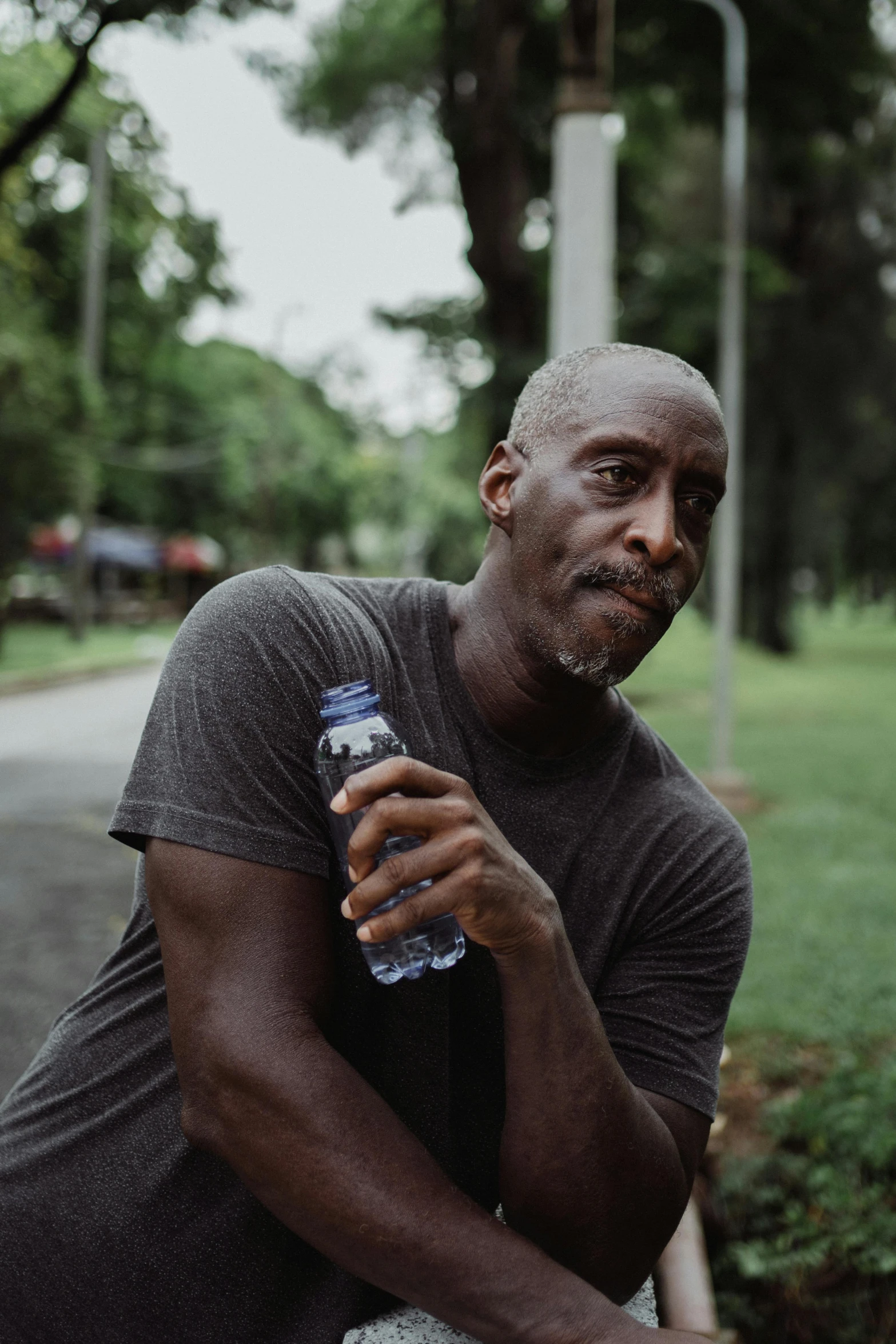 a man sitting on a bench holding a bottle of water, inspired by Phil Foglio, pexels contest winner, happening, man is with black skin, mature male, profile pic, sweating