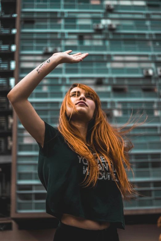 a woman with red hair standing in front of a building, inspired by Elsa Bleda, pexels contest winner, raising an arm, wearing a black shirt, young woman looking up, performing