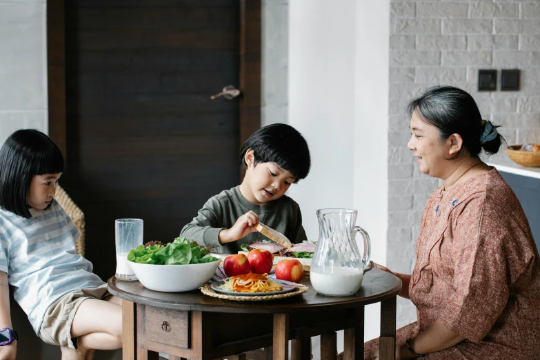 a group of people sitting around a table eating food, with a kid, bowl filled with food, background image, darren quach