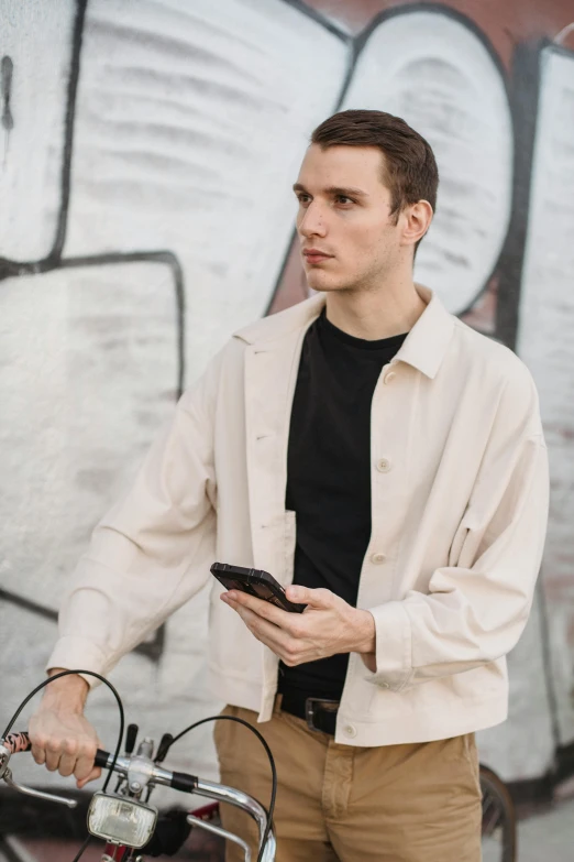 a man standing next to a bike holding a cell phone, trending on pexels, bauhaus, wearing a linen shirt, wearing off - white style, short jacket, promotional image