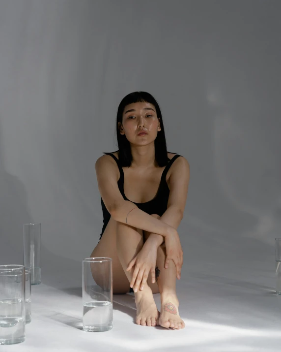 a woman sitting on the floor next to a glass of water, inspired by Kim Tschang Yeul, trending on unsplash, hyperrealism, non binary model, stood in a lab, photoshoot for skincare brand, asian human