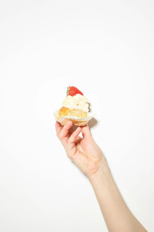 a person holding a cupcake in their hand, by Eva Frankfurther, minimalism, pose 4 of 1 6, toast, holding a giant strawberry, cream white background