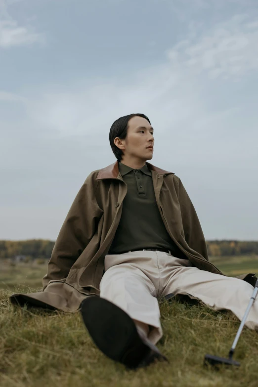 a man sitting in the grass with a golf club, an album cover, by Attila Meszlenyi, unsplash, visual art, wearing a turtleneck and jacket, androgynous person, inuit heritage, looking away