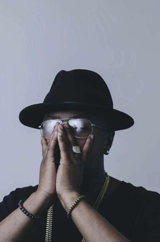 a man in a hat and glasses covers his face with his hands, an album cover, inspired by Zhu Da, unsplash, notorious b i g, low quality photo, profile photo, rapper bling jewelry