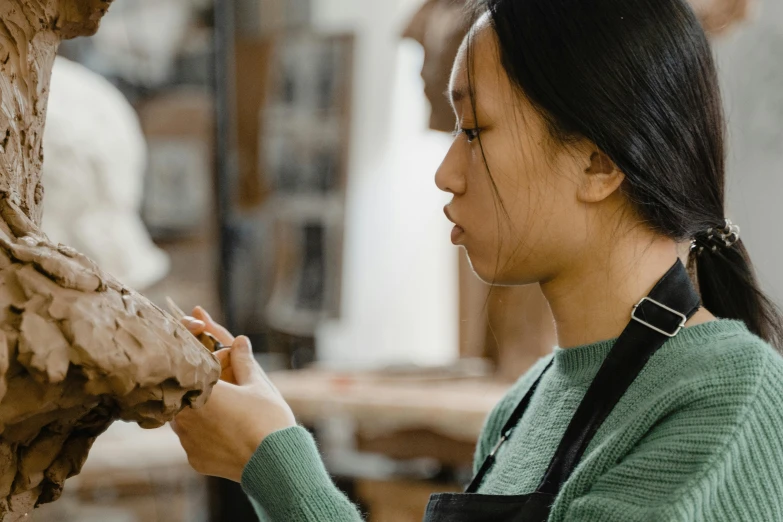 a woman is working on a clay sculpture, trending on pexels, academic art, young asian girl, profile image, holding a wood piece, anthro