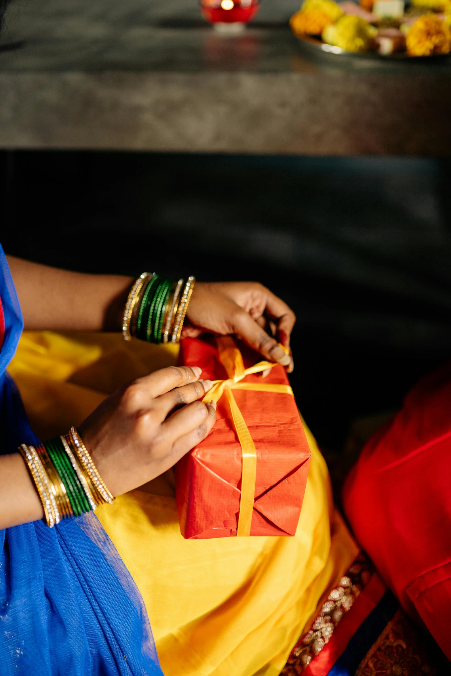 a woman sitting on a couch holding a gift, pexels contest winner, hurufiyya, red and blue garments, yellow and blue ribbons, india, square