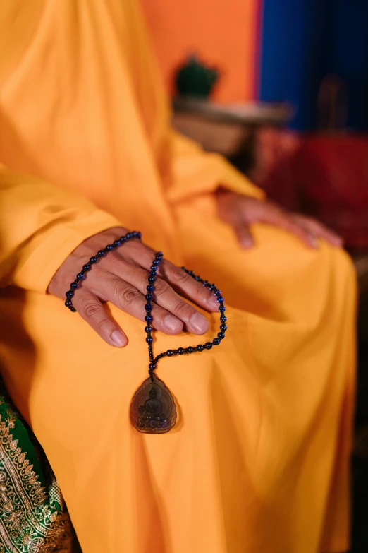 a close up of a person holding a rosary, inspired by Tang Di, hurufiyya, yellow, anjali mudra, medium-shot, indigo