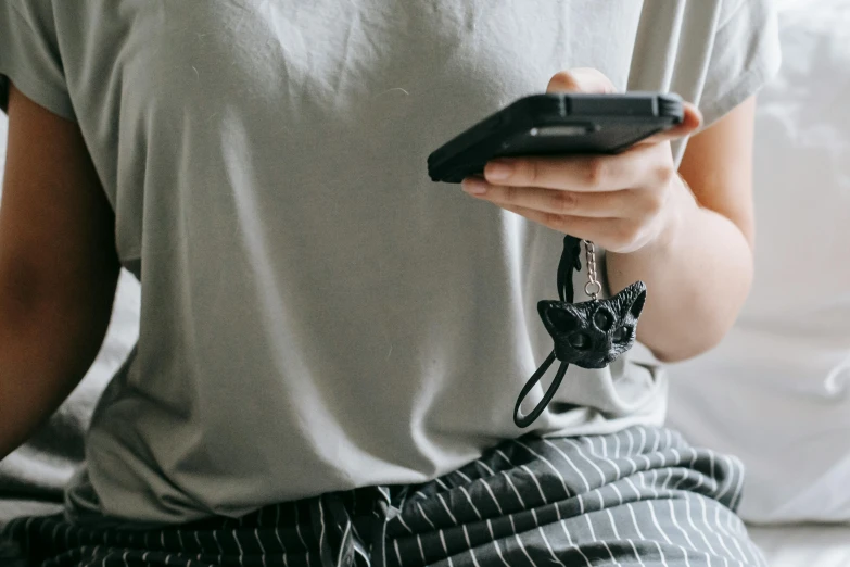 a woman sitting on a bed holding a cell phone, a cartoon, trending on pexels, shungite bangle, wearing a cropped tops, black and grey, a telephone receiver in hand