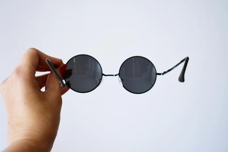 a close up of a person holding a pair of sunglasses, by Bernie D’Andrea, trending on unsplash, photorealism, huge black circle, long trunk holding a wand, on grey background, hippie