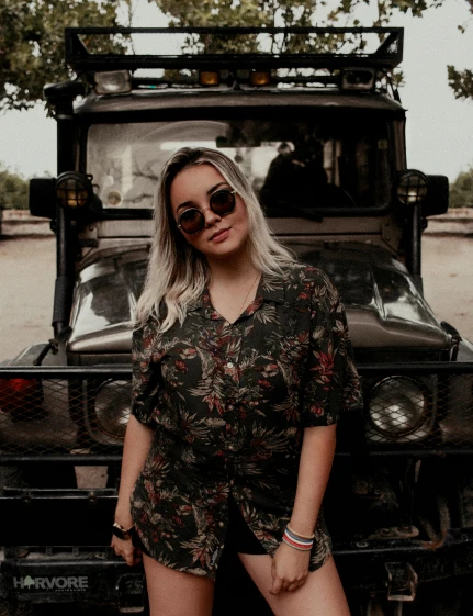 a woman standing in front of a jeep, an album cover, trending on unsplash, jungle camo, low quality photo, wearing shades, she is mexican
