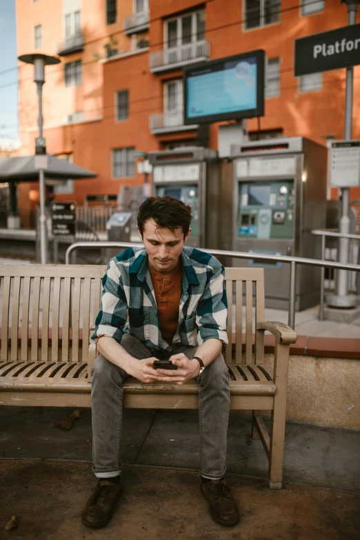 a man sitting on top of a wooden bench, holds a smart phone in one hand, looking distracted, non-binary, square