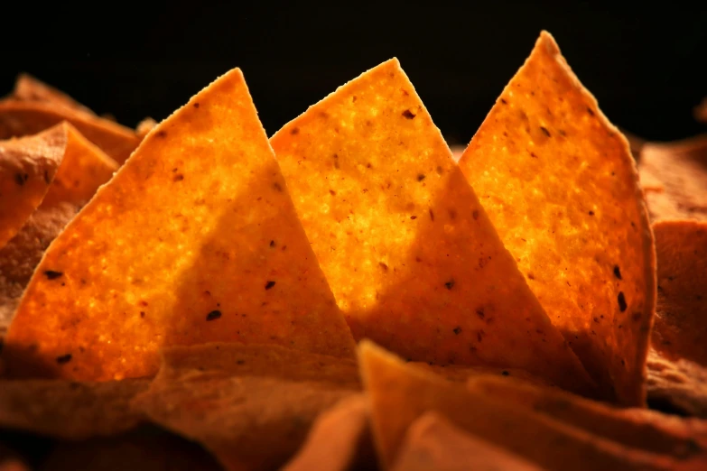 a pile of tortilla chips sitting on top of a table, by Carey Morris, pexels, photorealism, orange light, triangles, taco, lighting chiaroscuro