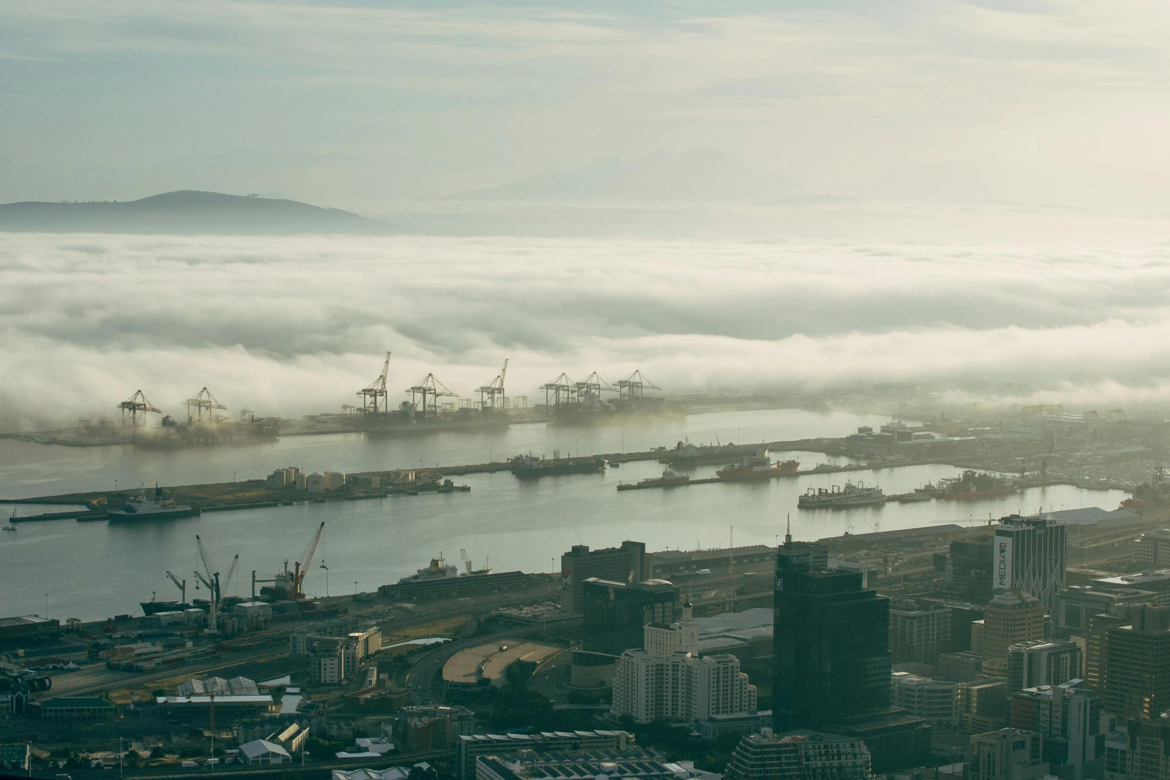 a city filled with lots of tall buildings next to a body of water, by Daniel Lieske, pexels contest winner, hurufiyya, in the bottom there a lot of fog, shipping docks, south african coast, port scene background