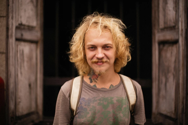 a close up of a person with a backpack, a character portrait, inspired by Thomas Gambier Parry, pexels contest winner, messy blond hair, tattooed man, wide forehead, very slightly smiling