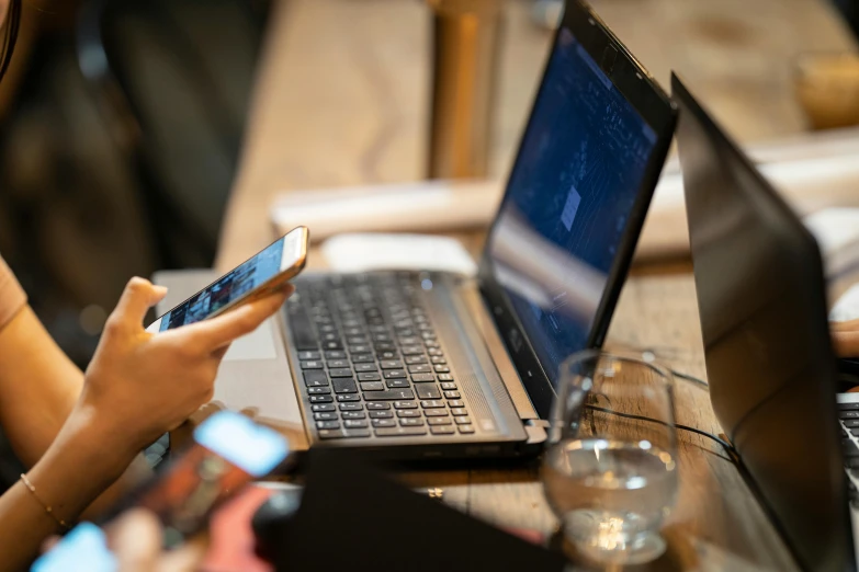 a woman sitting at a table with a laptop and a cell phone, pexels, happening, middle shot, thumbnail, coding, multiple stories