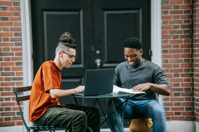 two men sitting at a table with a laptop, by Carey Morris, trending on pexels, renaissance, teenage boy, background image, mix of ethnicities and genders, lachlan bailey