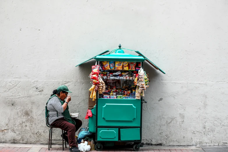 a man sitting on a chair in front of a vending machine, by Alejandro Obregón, pexels contest winner, street art, neo - andean architecture, square, cart, teal