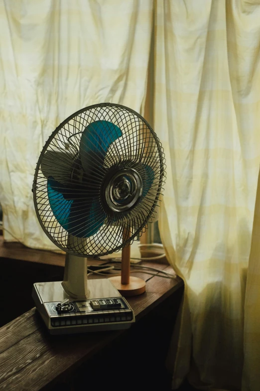 a fan sitting on top of a wooden table next to a window, photorealism, color photograph, blue, cooling, gold