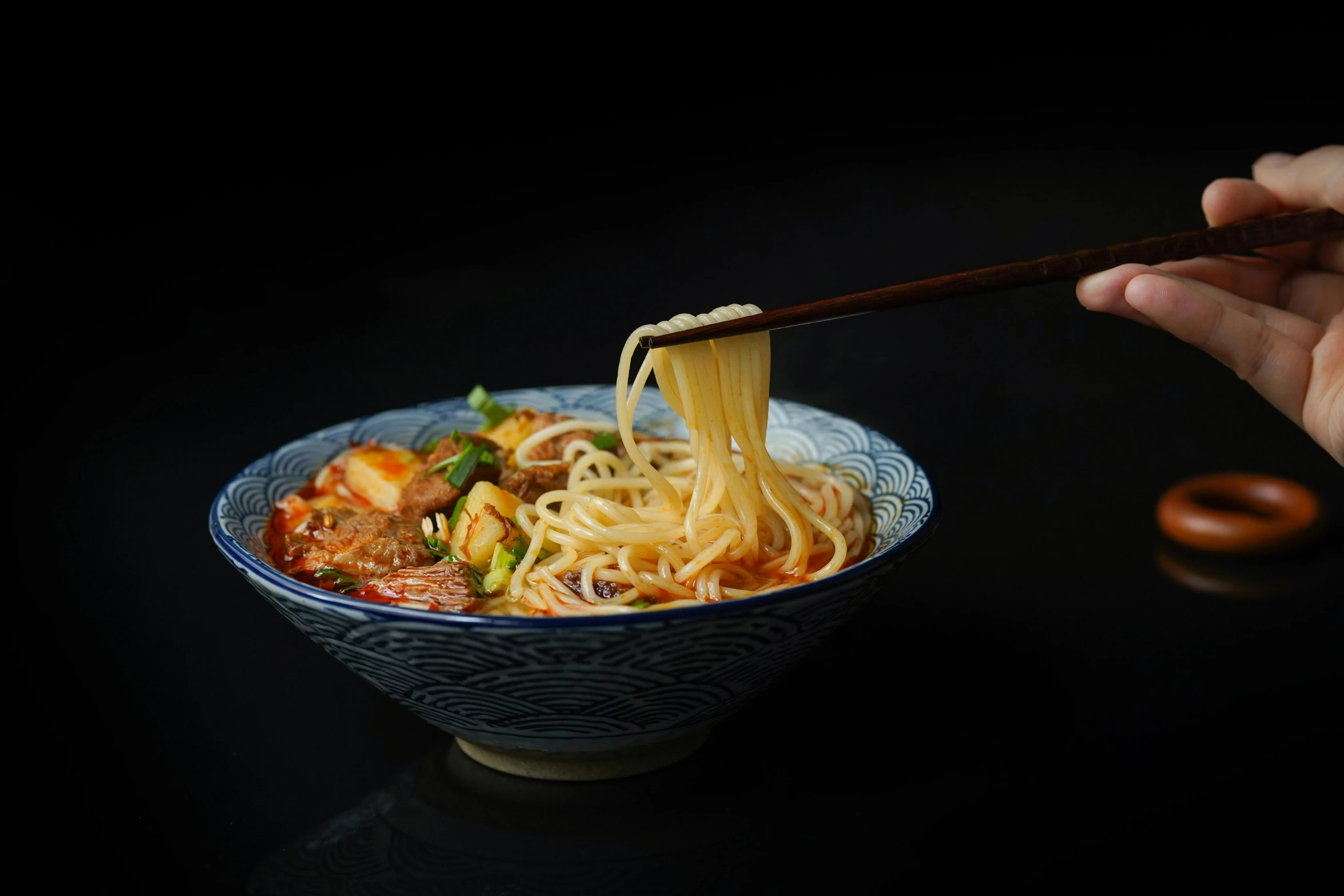 a person holding chopsticks over a bowl of noodles, inspired by Wang Mian, with a black background, ruanjia, plated arm, product introduction photo