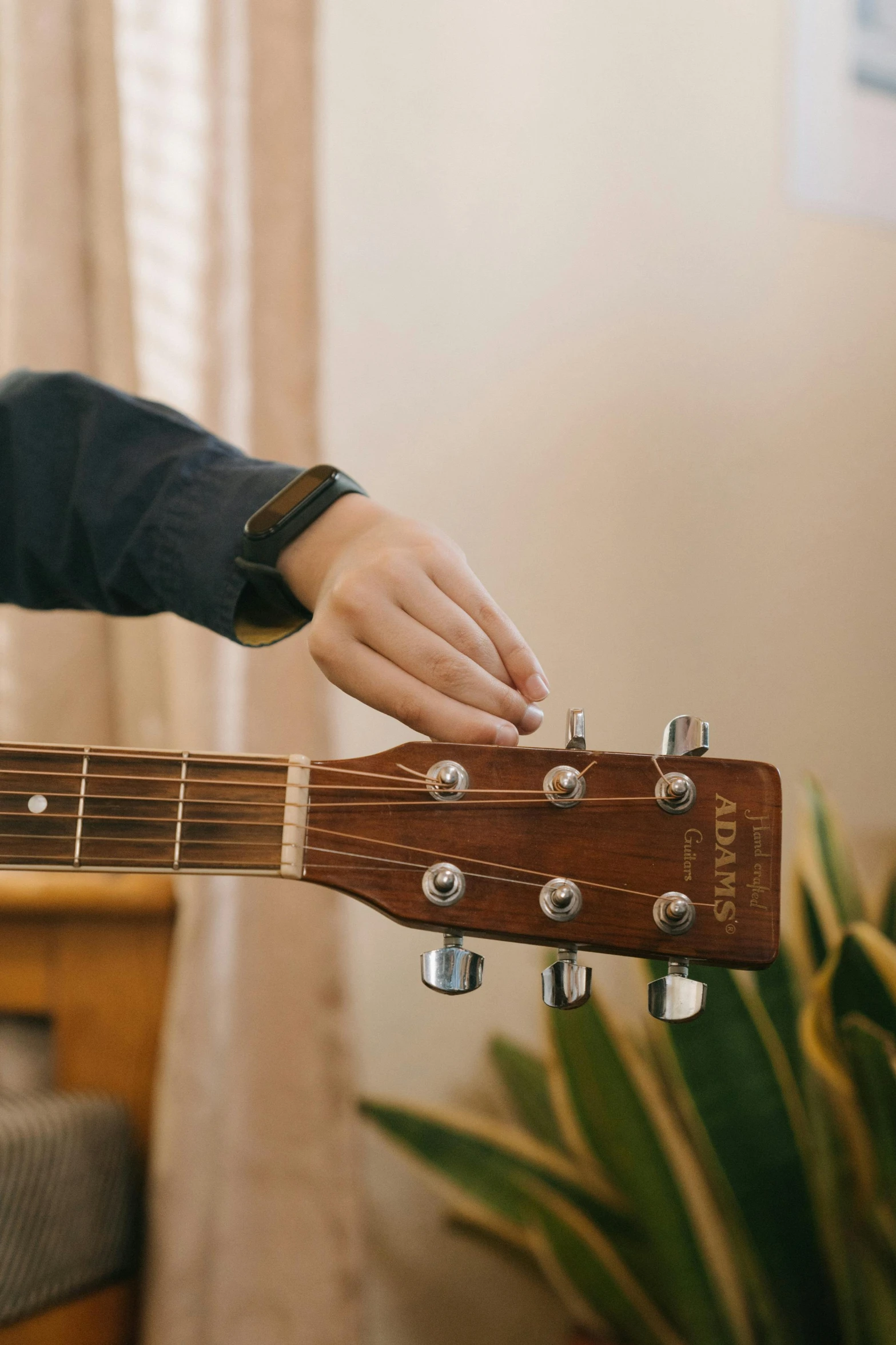 a close up of a person playing a guitar, home setting, instructions, wears a watch, sydney hanson