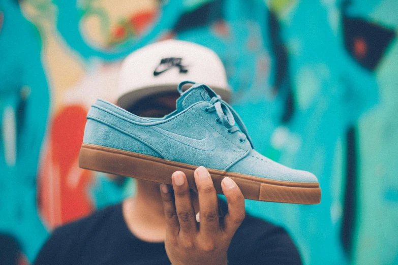 a person holding a blue shoe in front of a graffiti wall, trending on unsplash, wearing a light blue shirt, a wooden, snacks, hand holding cap brim