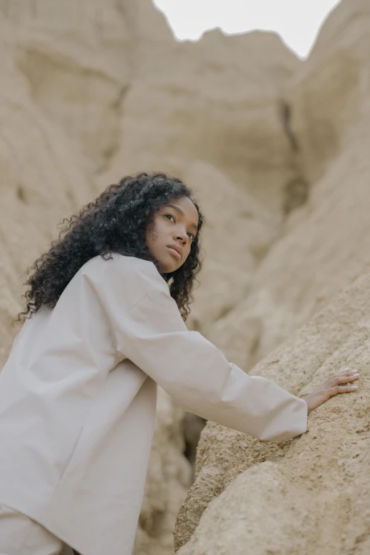 a woman leaning on a rock in the desert, an album cover, trending on unsplash, visual art, wearing lab coat and a blouse, wearing a track suit, a black man with long curly hair, full frame image