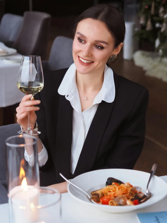 a woman sitting at a table with a plate of food and a glass of wine