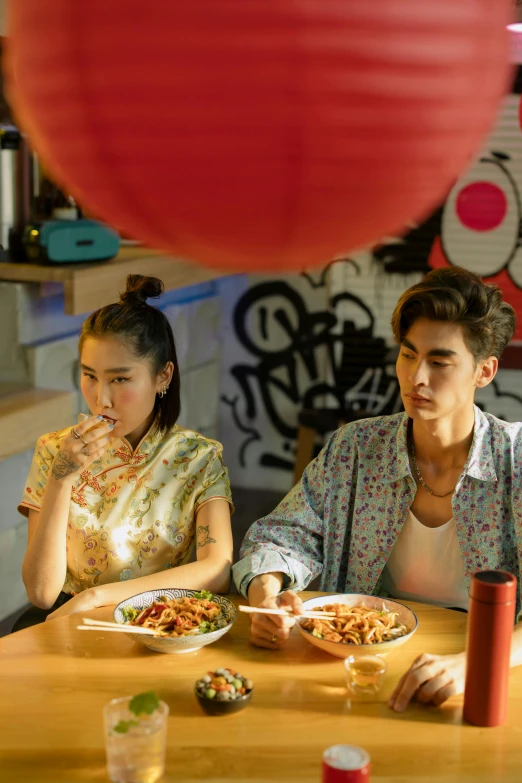 two people sitting at a table with plates of food, a picture, inspired by Lu Guang, trending on pexels, city hunter, looking off to the side, red lanterns, young asian woman