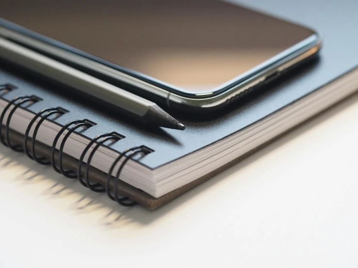 a cell phone sitting on top of a notebook, by Robbie Trevino, trending on pexels, photorealism, black, closeup - view, sleek spines, educational supplies