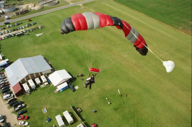 a group of people standing on top of a lush green field, skydiving, black and red scheme, overhead canopy, whealan