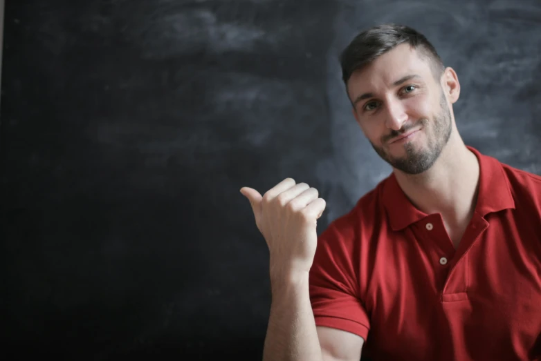 a man in a red shirt sitting in front of a blackboard, pexels contest winner, pointing index finger, handsome young man, h3h3, smileing nright
