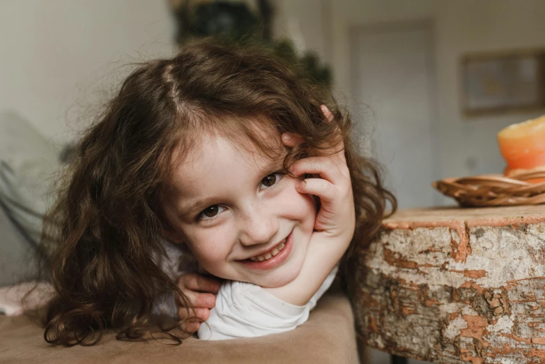 a little girl laying on top of a couch, by Emma Andijewska, pexels contest winner, happening, detailed smile, brown curly hair, hand on cheek, 4yr old