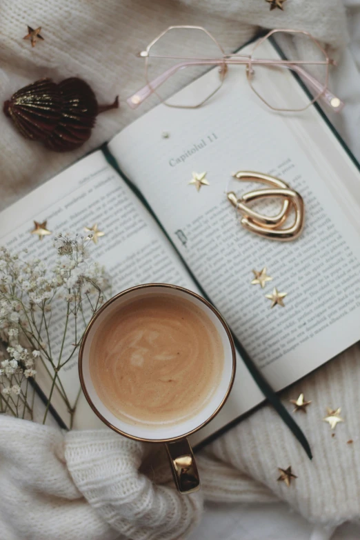 an open book sitting on top of a bed next to a cup of coffee, a still life, by Julia Pishtar, pexels contest winner, tiny stars, white and gold color palette, latte art, photo of a model