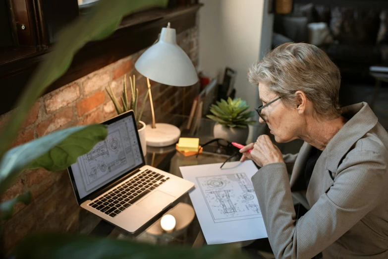 a woman sitting at a desk in front of a laptop, a detailed drawing, by Jessie Algie, pexels contest winner, architect, middle - age, 9 9 designs, working on her laptop