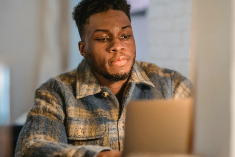 a man sitting in front of a laptop computer, by Carey Morris, trending on pexels, renaissance, ( ( dark skin ) ), boy with neutral face, early in the morning, serious focussed look