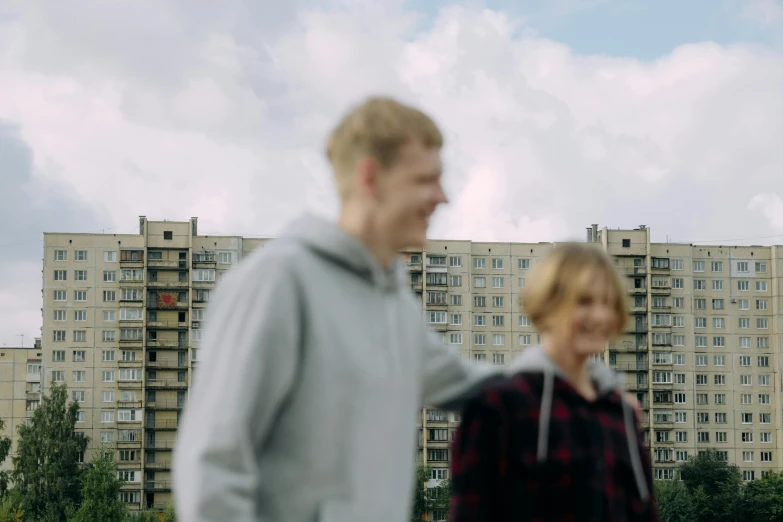 a man and a woman standing in front of a tall building, by Attila Meszlenyi, happening, teenage boy, 4 k film still, in a suburb, excited russians