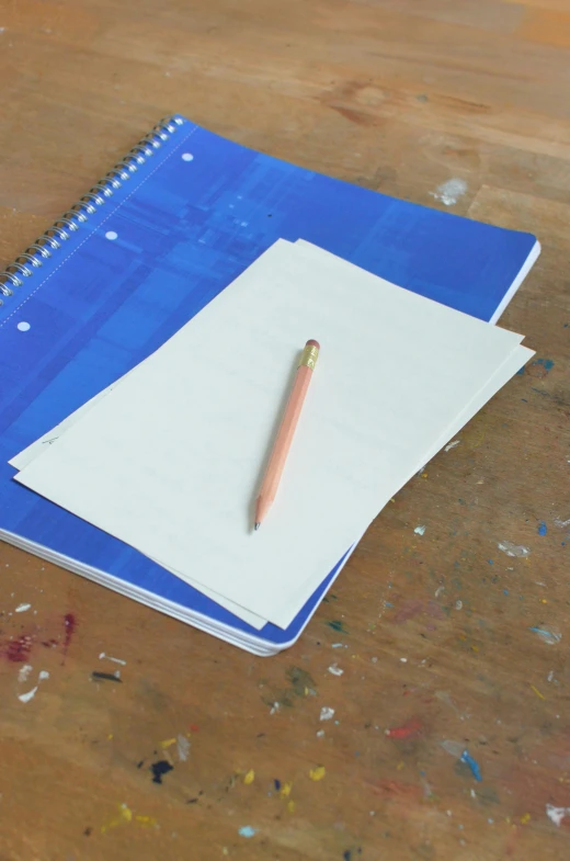 a blue notebook sitting on top of a wooden table, a child's drawing, by David Simpson, visual art, holding pencil, 100lb cardstock, parchment, unfinished