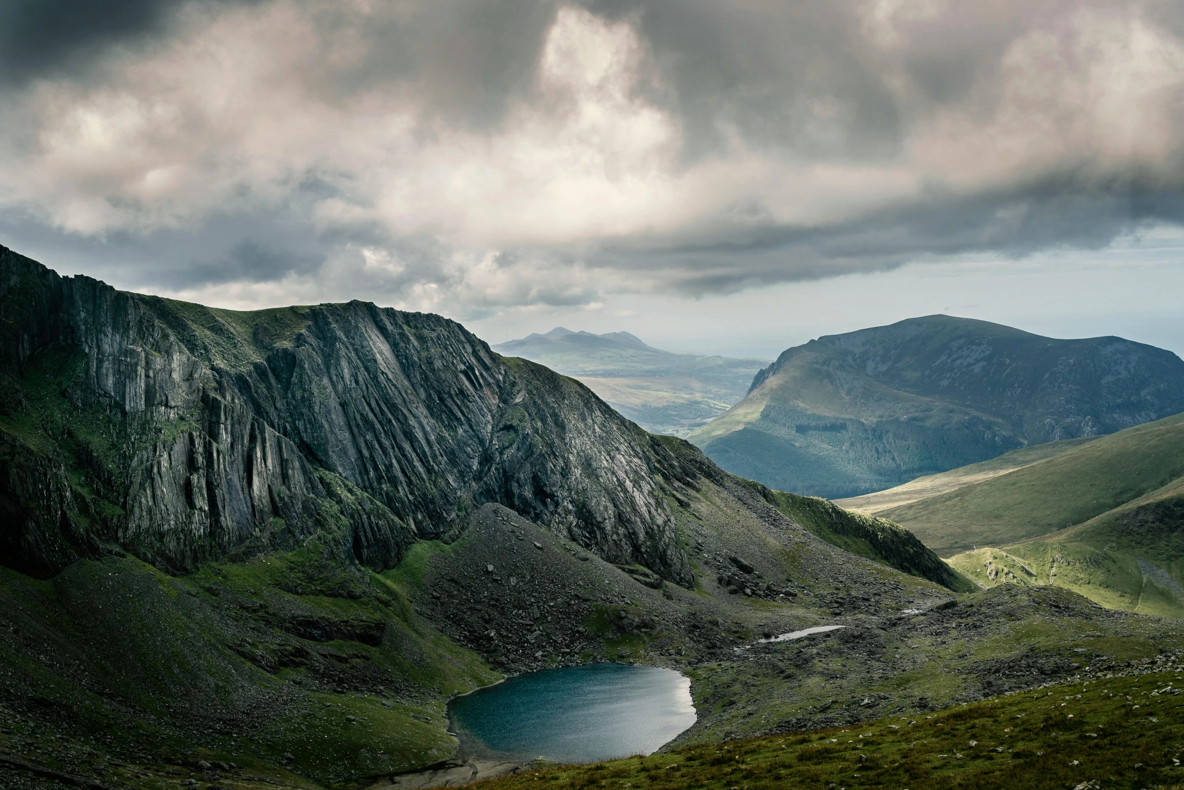 a large body of water sitting on top of a lush green hillside, a detailed matte painting, by Bedwyr Williams, unsplash contest winner, craggy mountains, slate, irish mountains background, grey