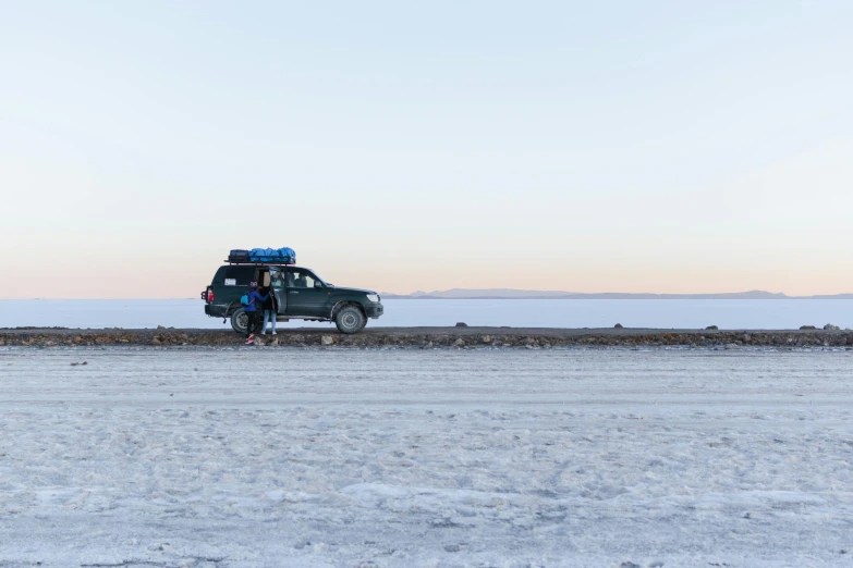 a car parked on top of a snow covered field, by Alexander Runciman, at salar de uyuni, people angling at the edge, profile image, 2 people