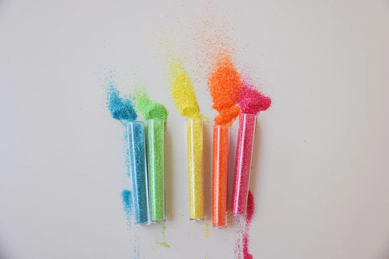 a group of colored pencils sitting on top of a white surface, a stipple, inspired by George Aleef, made out of sweets, blaster fire bright as neon, sand particles, 3 mm