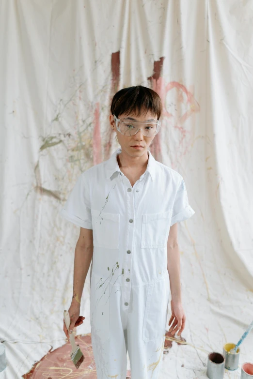 a boy that is standing in front of some paint, an album cover, inspired by Yeong-Hao Han, unsplash, gutai group, wearing a white button up shirt, painted overalls, jingna zhang, genderless
