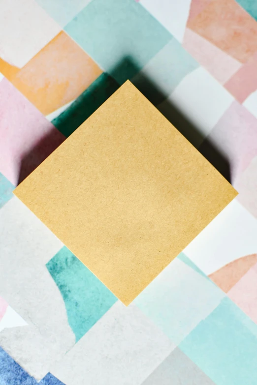 a piece of paper sitting on top of a table, an album cover, by Julia Pishtar, trending on unsplash, geometric abstract art, relaxed. gold background, square, diamond, pastel texture