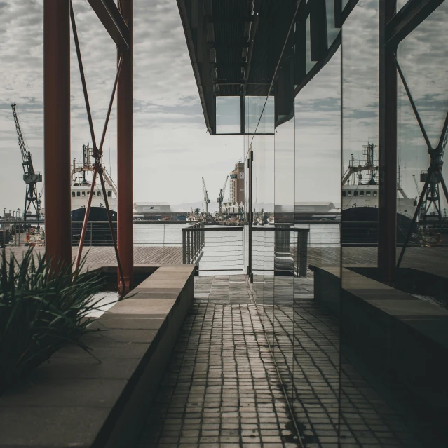 a walkway in front of a building next to a body of water, by Jacob Toorenvliet, pexels contest winner, modernism, ships in the harbor, view from inside, grey warehouse background, full frame image