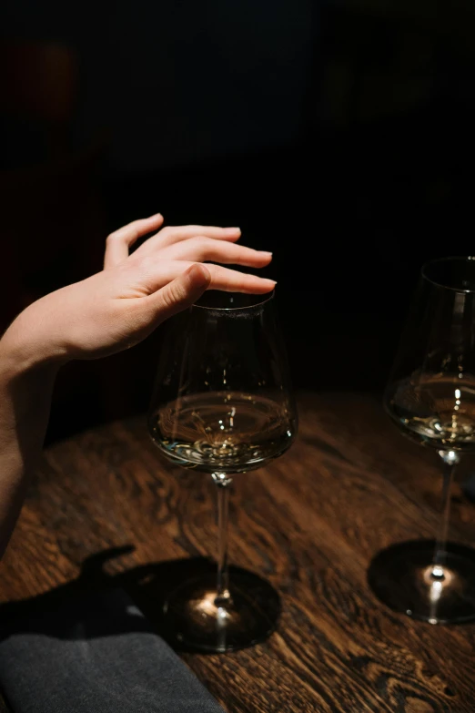 a woman sitting at a table with two wine glasses, inspired by Elsa Bleda, trending on unsplash, renaissance, hand gesture, nightlife, close-up of thin soft hand, hovering indecision