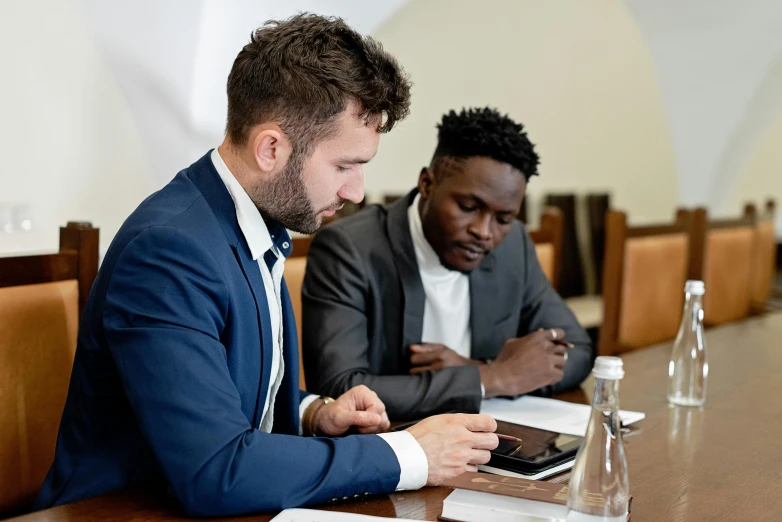 two men sitting at a table looking at a cell phone, pexels contest winner, in a business suit, varying ethnicities, coloured, schools